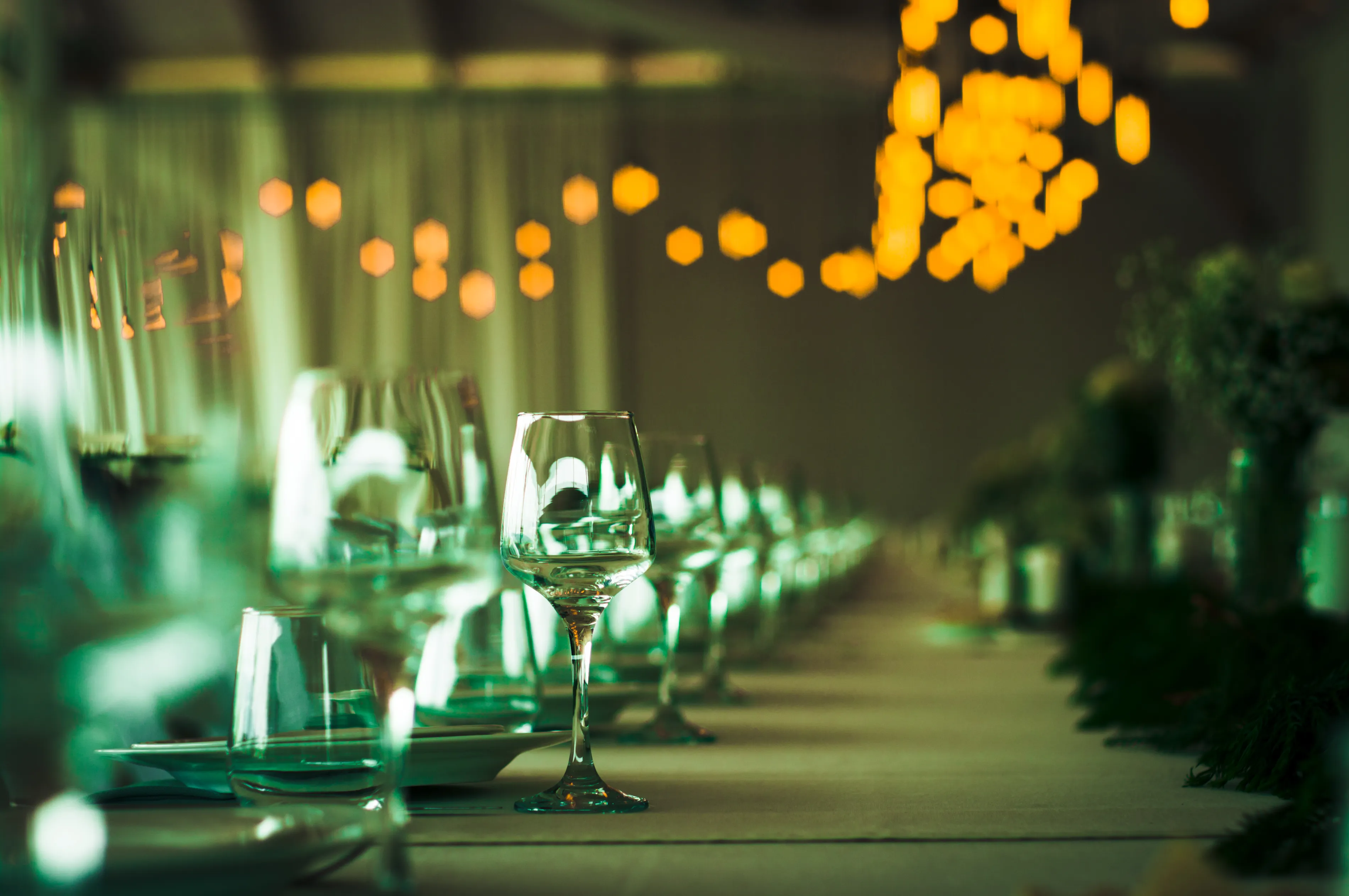 A long banquet table set with glassware under warm string lights