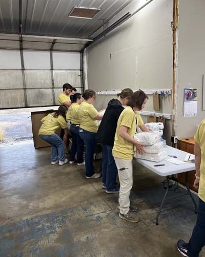 Volunteers in yellow shirts sorting and packing supplies in a warehouse bay