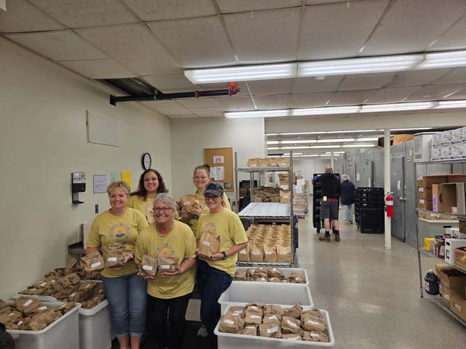 Five volunteers holding packed lunch bags in a food pantry work room