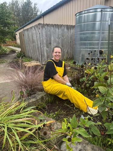 A volunteer in yellow rain overalls taking a break in a landscaped garden bed