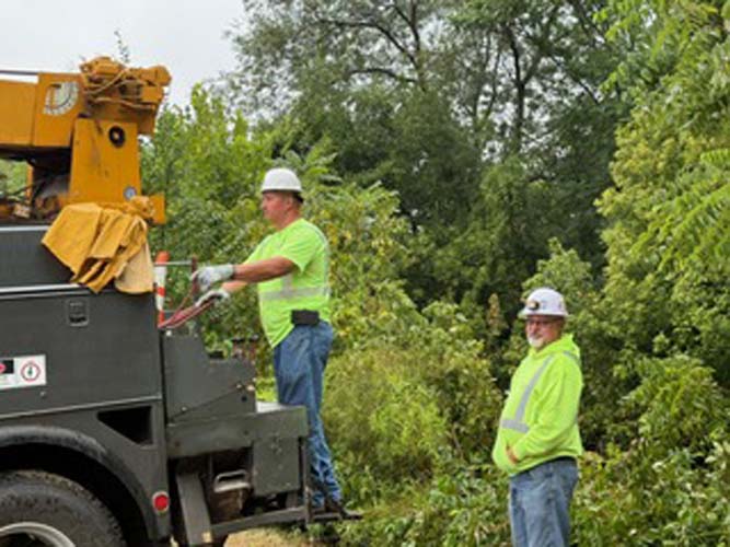 Two utility line workers clearing brush from a bucket truck