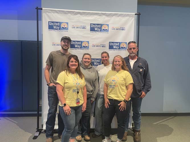 A team of seven volunteers posing together at the United Way banner