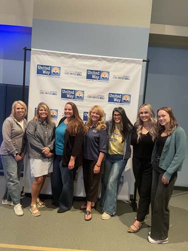 Seven volunteers posing together at the United Way banner
