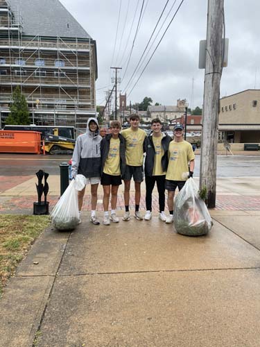 Five student volunteers with bags of collected litter on a downtown sidewalk