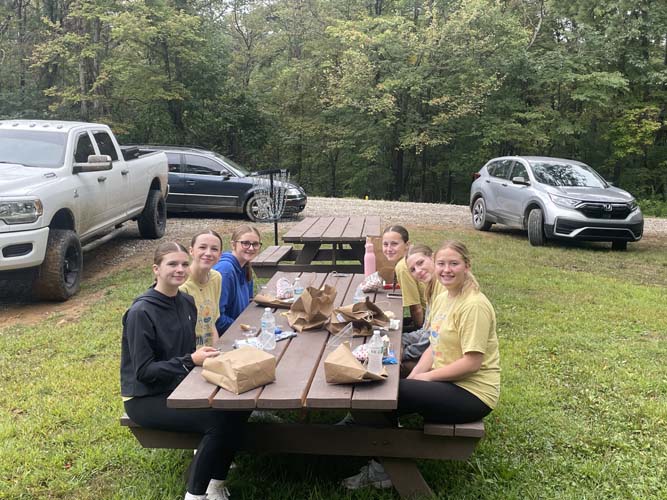 Student volunteers eating packed lunches at a picnic table in the woods