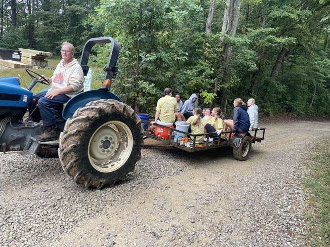 A tractor pulling a wagon of volunteers along a gravel drive