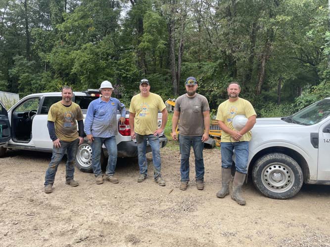 Five work crew volunteers posing beside their trucks at a rural site