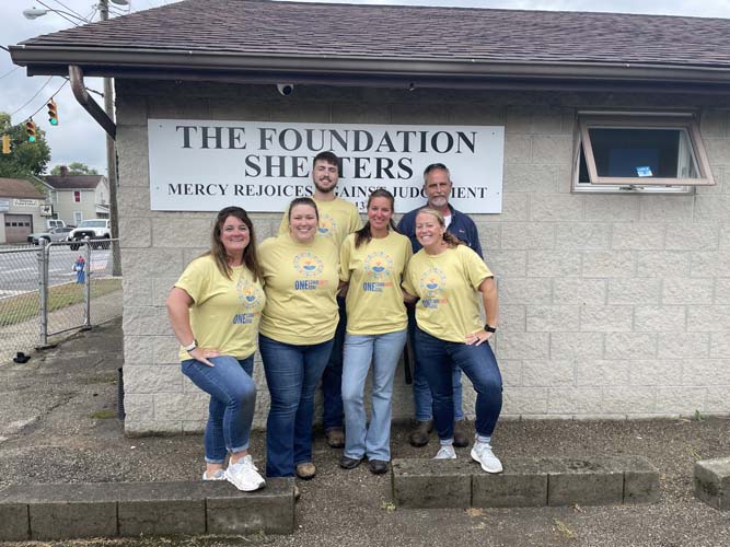Five volunteers posing in front of The Foundation Shelters sign