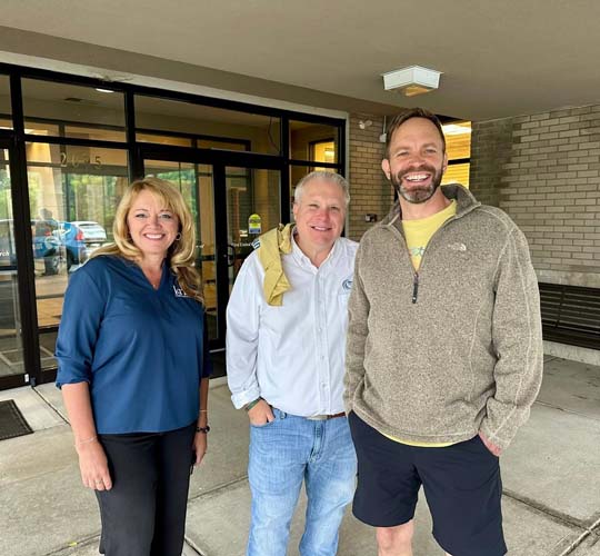 Three volunteers posing outside a building entrance