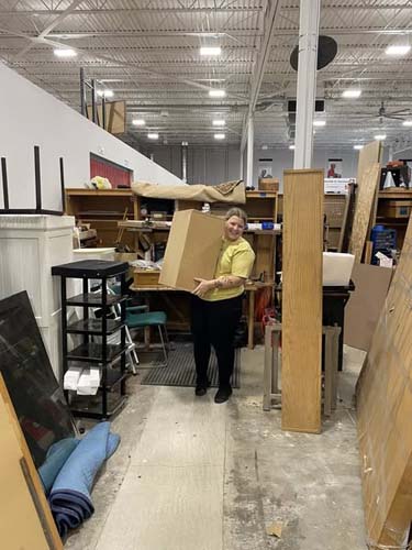 A volunteer carrying a large box through a furniture warehouse