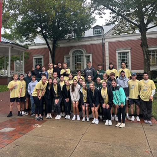 A large group of student volunteers posing outside a brick building