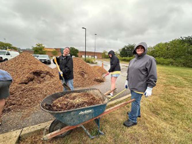 Volunteers shoveling mulch into wheelbarrows in a parking lot