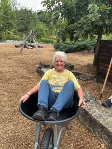 A volunteer sitting in a wheelbarrow after finishing a playground project