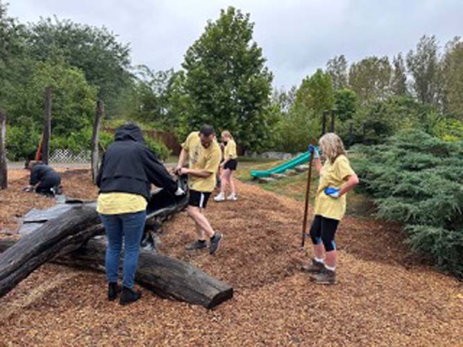Volunteers spreading mulch near a playground slide