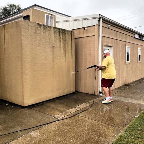 A volunteer power washing the exterior wall of a building