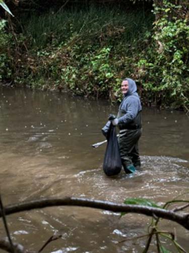 A volunteer in waders pulling trash from a creek