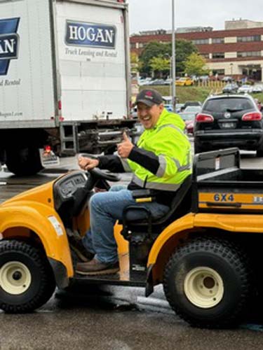 A worker giving a thumbs up from a utility cart beside a moving truck