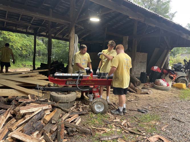 Three volunteers operating a log splitter under a barn shelter