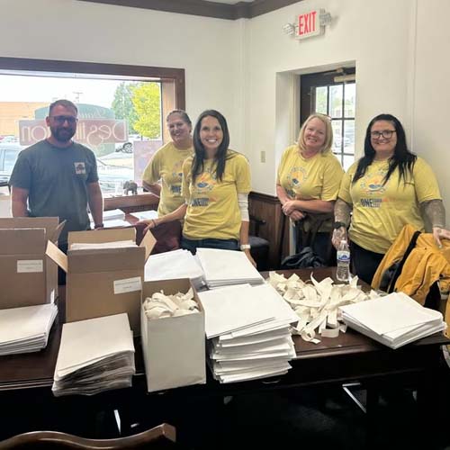 Five volunteers packing envelopes at a long table