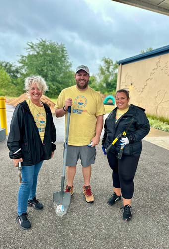 Three volunteers with a shovel posing outside a project site