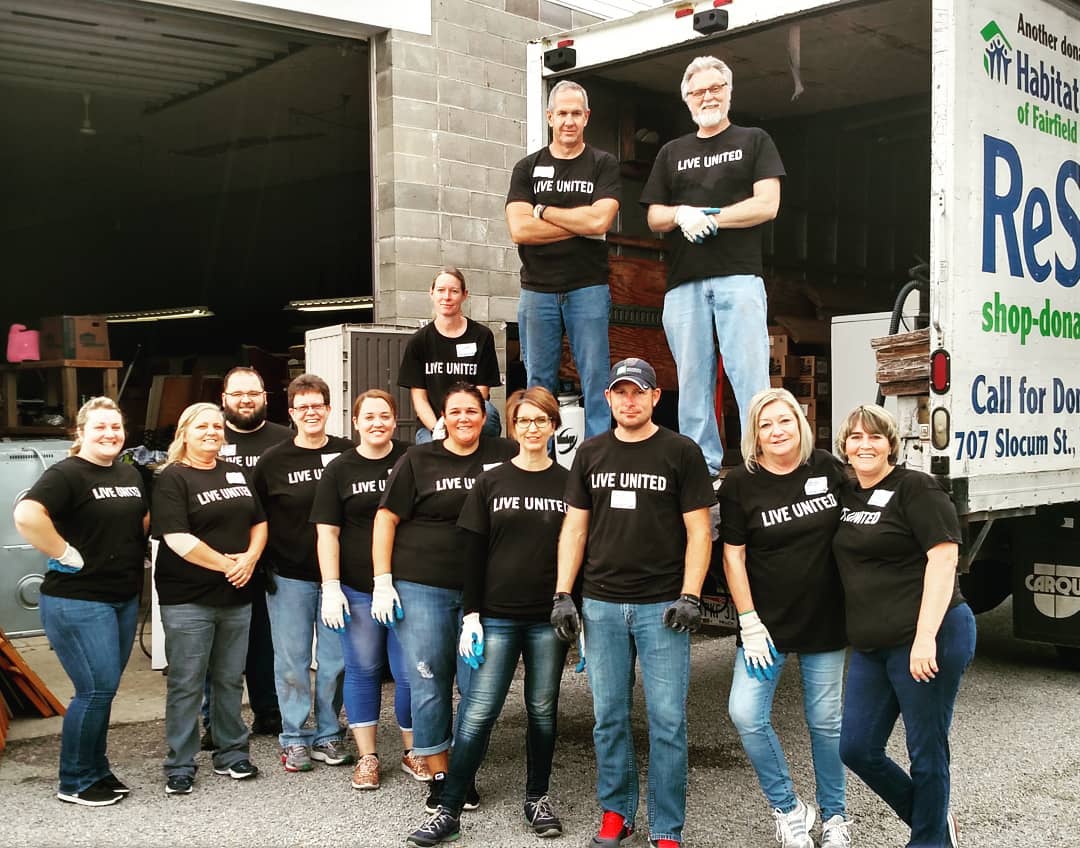 A team of volunteers in LIVE UNITED shirts posing in front of a Habitat ReStore truck