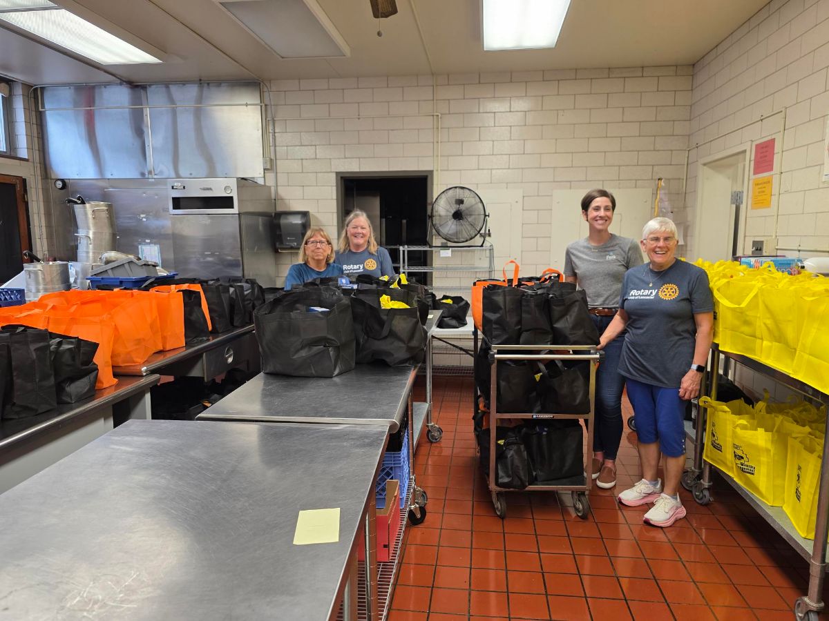 Four Rotary Club of Lancaster volunteers with carts and tables of packed orange, black and yellow bags