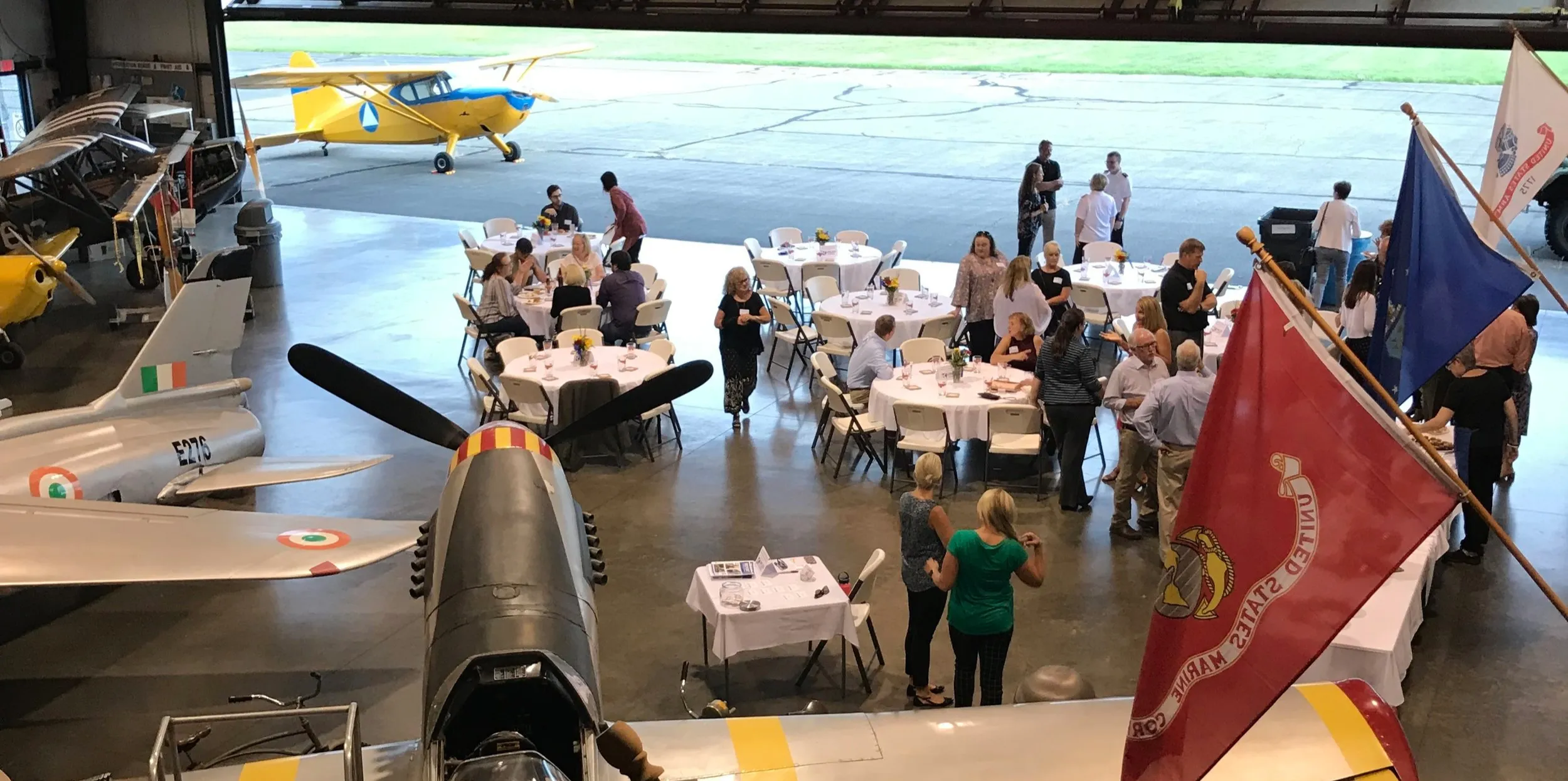 Guests mingling at round tables in an aircraft hangar at a past Pillars reception