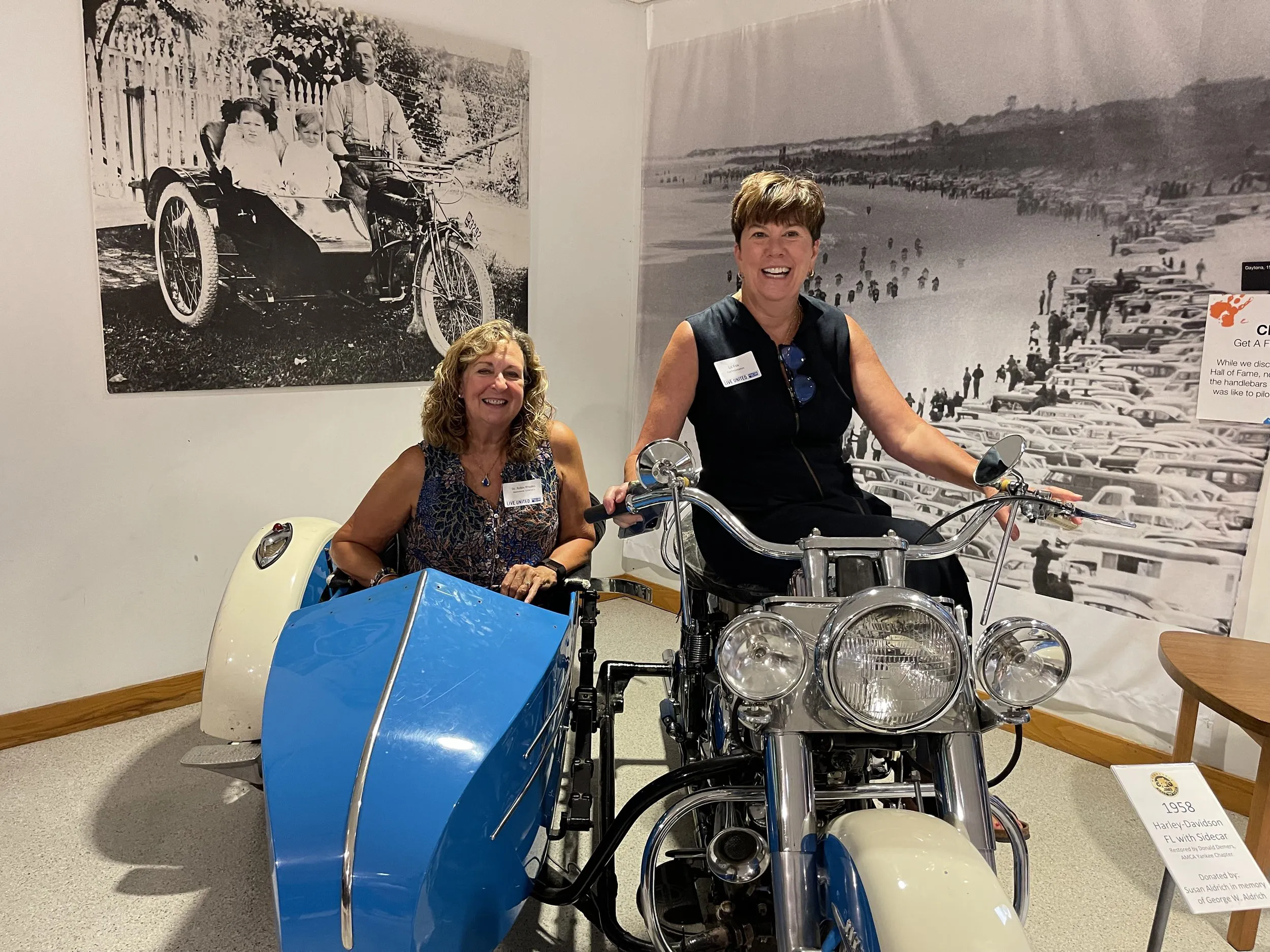 Two attendees smiling beside the motorcycle exhibit