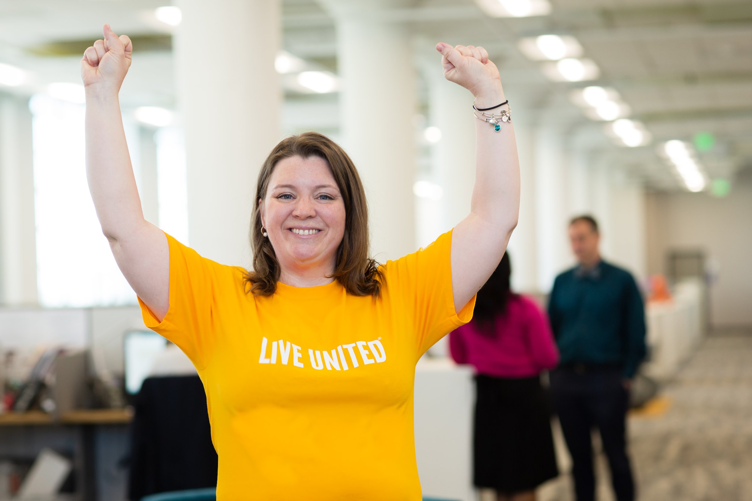 A United Way supporter in a LIVE UNITED shirt cheering with both arms raised in an office